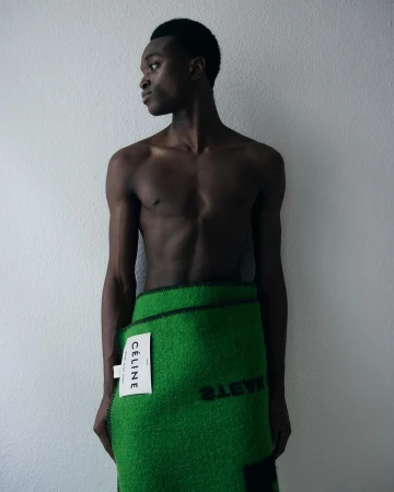 Shirtless black man wrapped in a green textured fabric towel against a white textured wall