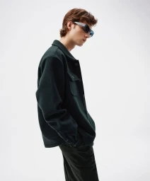 Young man in dark green shirt and sunglasses posing against a plain white background by Quirin Siegert in Berlin.