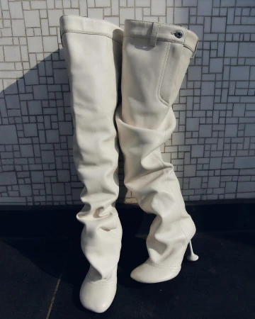 Close-up portrait of white over-the-knee leather heeled boots standing against a light tiled wall in Berlin by Quirin Siegert.