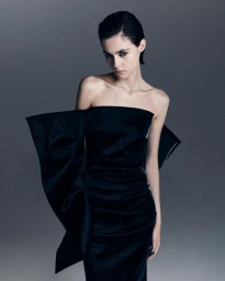 Woman in a strapless black satin dress with dramatic flared sides against a grey background
