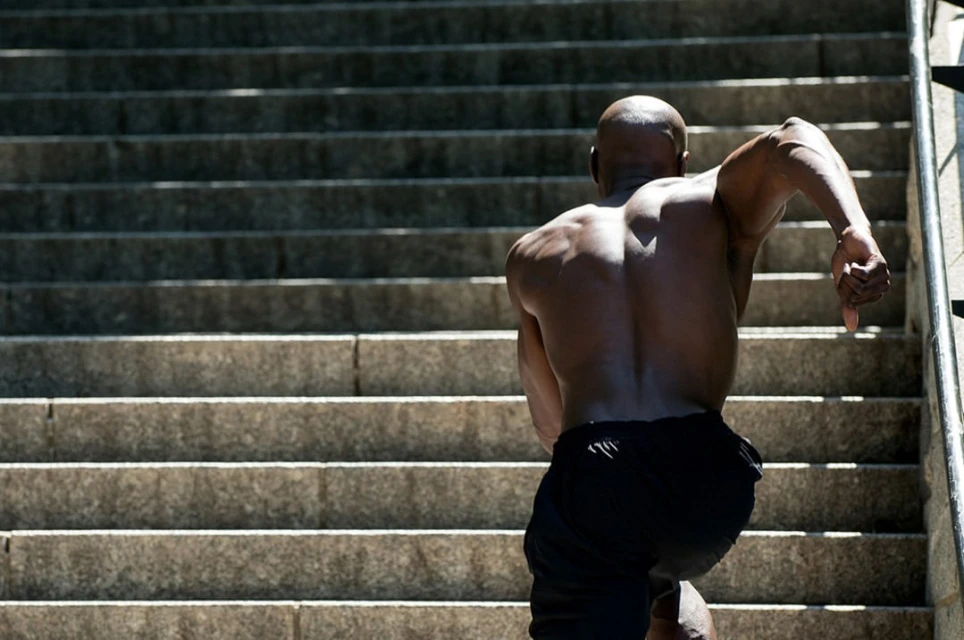 African American adult male running up the steps outdoors. Close-up, rear view of bald muscular man exercising on concrete stairs in daylight.
