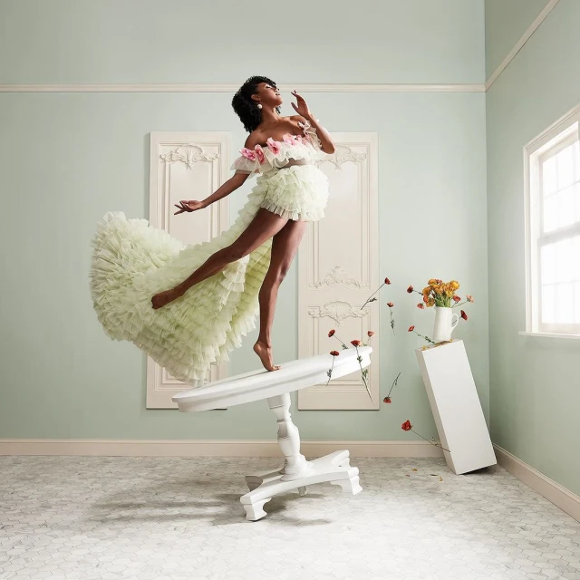 An African American woman in an elaborate, light green dress dances on a white table in a room with light blue walls and white trim.