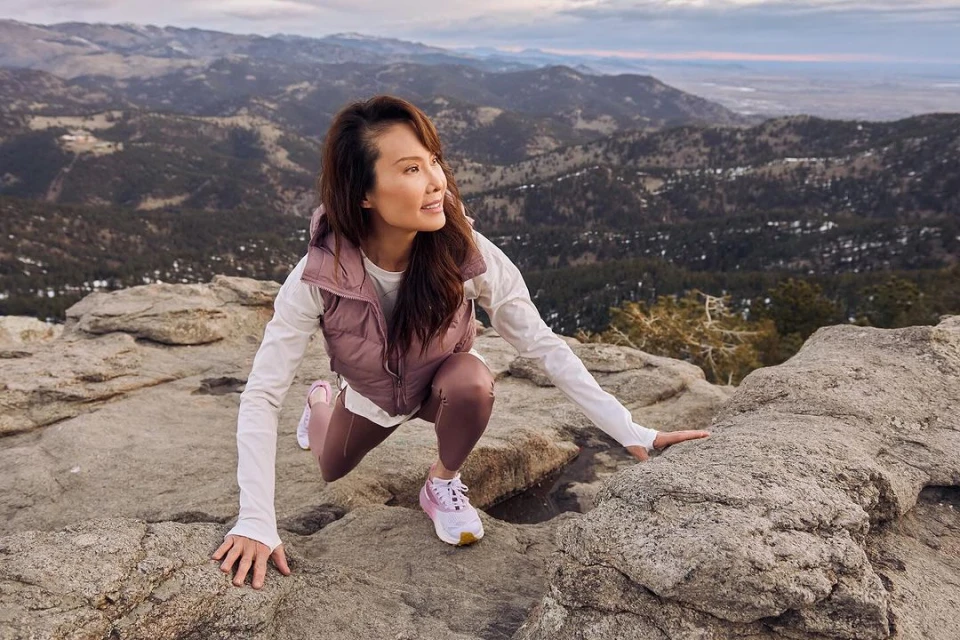 Adult woman on a mountain peak in athletic wear pauses while hiking to enjoy the view on a sunny day with mountains in the background.
