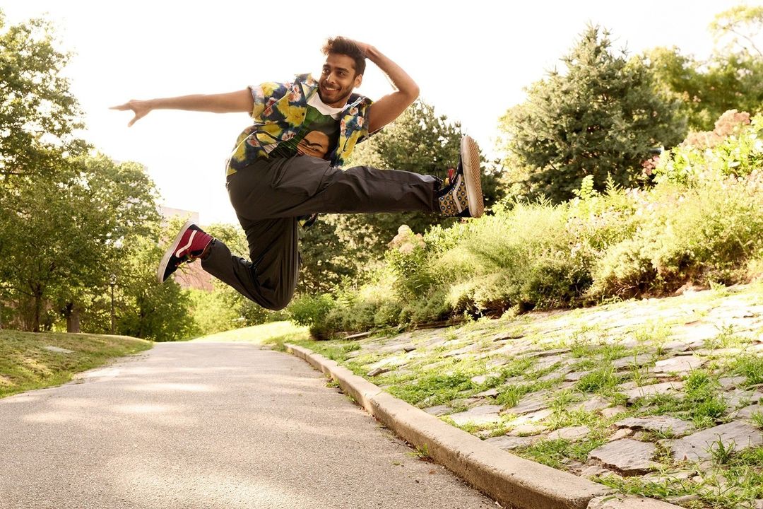 Man in floral shirt jumps on park path; joyful action shot captures movement, lush greenery, athletic pose, and vibrant style.