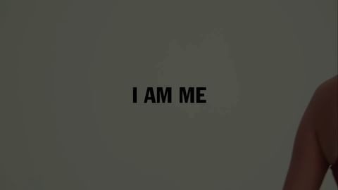 Upper torso of adult woman with shoulders, chest, and arm visible against grey background with black text reading 'I AM ME.'