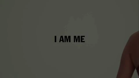 Upper torso of adult woman with shoulders, chest, and arm visible against grey background with black text reading 'I AM ME.'