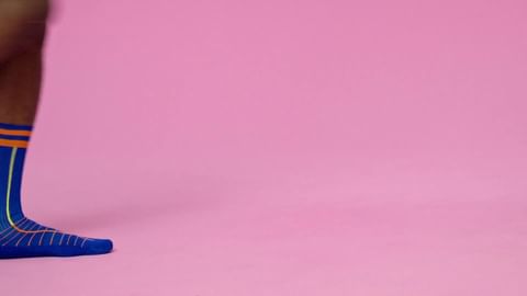 Leg with blue and orange sock in a pink studio. Close up studio shot with a leg wearing a designed sock.