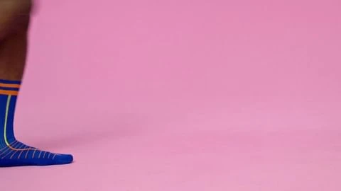 Leg with blue and orange sock in a pink studio. Close up studio shot with a leg wearing a designed sock.