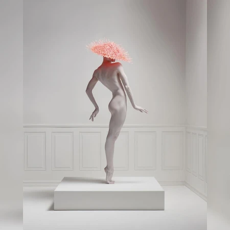 A nude adult woman stands on a white cube in a bright white studio with decorative wall panels, wearing a textured pink headpiece.