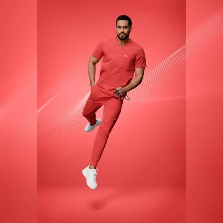 Adult male wearing red scrubs and white sneakers jumps against a red background with graphics. He holds glasses in his left hand.