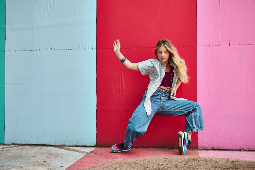 Blonde woman in casual clothes strikes a dynamic pose against a vibrant multicolored wall, showcasing a blend of fashion and urban style.