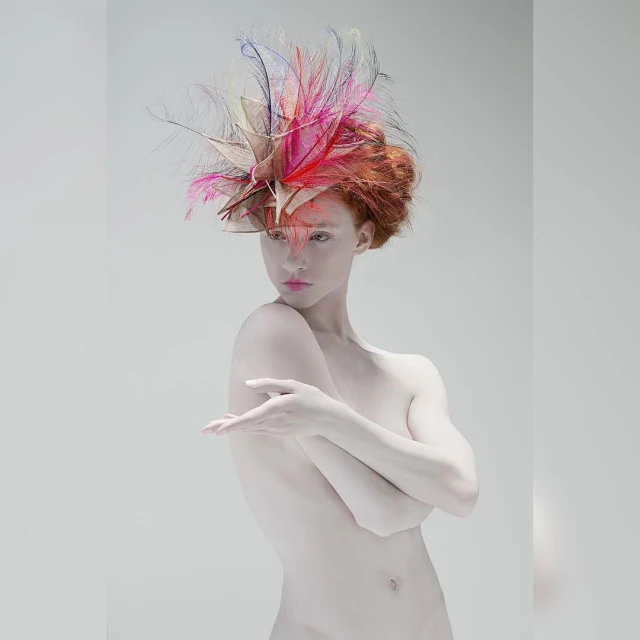Woman with pale skin and red hair wearing feathered headpiece in front of grey background. Fashion photography. Beauty shot.
