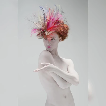 Woman with pale skin and red hair wearing feathered headpiece in front of grey background. Fashion photography. Beauty shot.