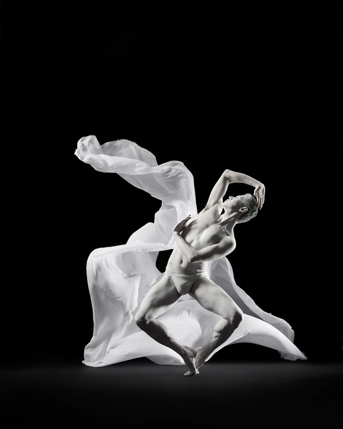 Dancer in dynamic pose with flowing white fabric against a solid black background by Rachel Neville