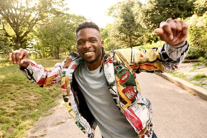 Smiling black man wearing a colorful patterned jacket dancing along a paved park path