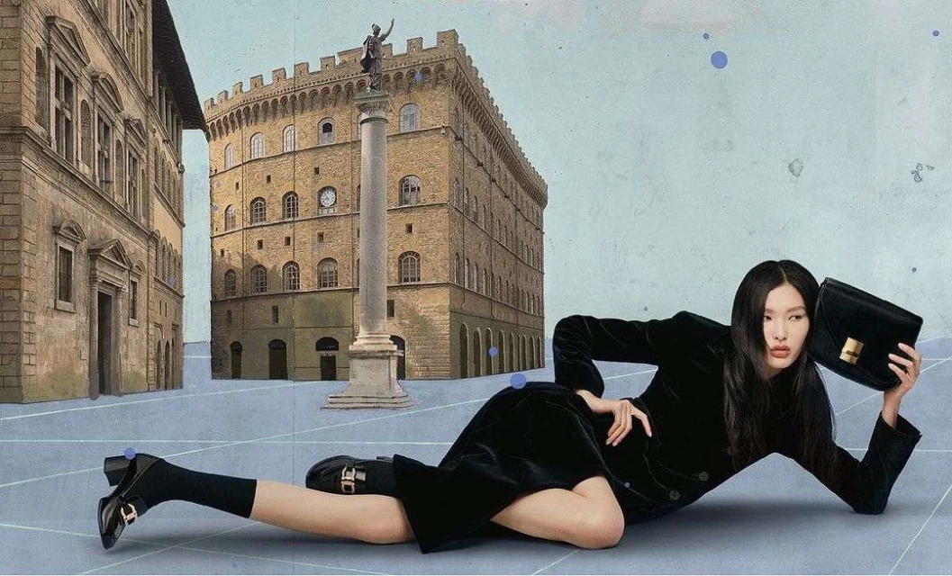 Fashion shot of an Asian female model reclining with a black purse, wearing a black velvet suit, with a European cityscape backdrop.