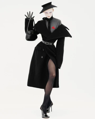 Fashion editorial shot of an adult female wearing a black coat, hat, gloves, and heels, posing with a black purse on a white background.