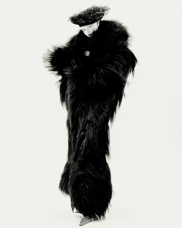 Full-length shot of a person wearing a furry black floor-length coat and matching hat, posing in a white studio setting.
