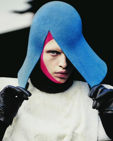 Model wearing a blue sculptural hat, pink face covering, and black leather gloves by photographer Rafael Pavarotti