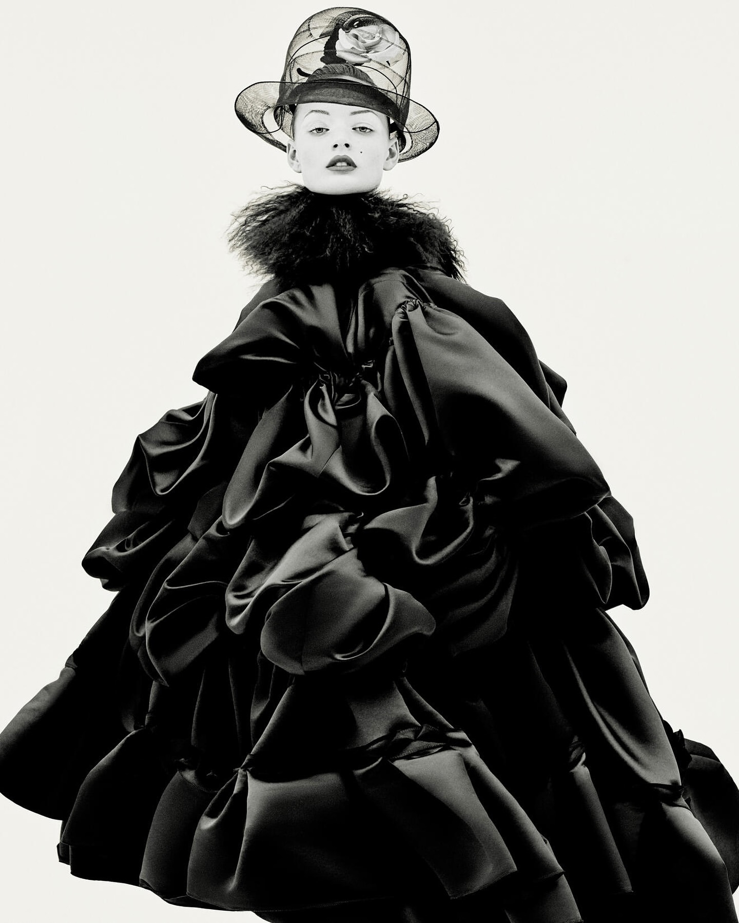 Fashionable adult female wearing elaborate ruffled black dress and artistic hat with a white studio background in a studio shot.