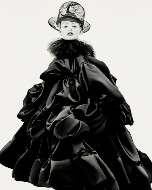 Fashionable adult female wearing elaborate ruffled black dress and artistic hat with a white studio background in a studio shot.