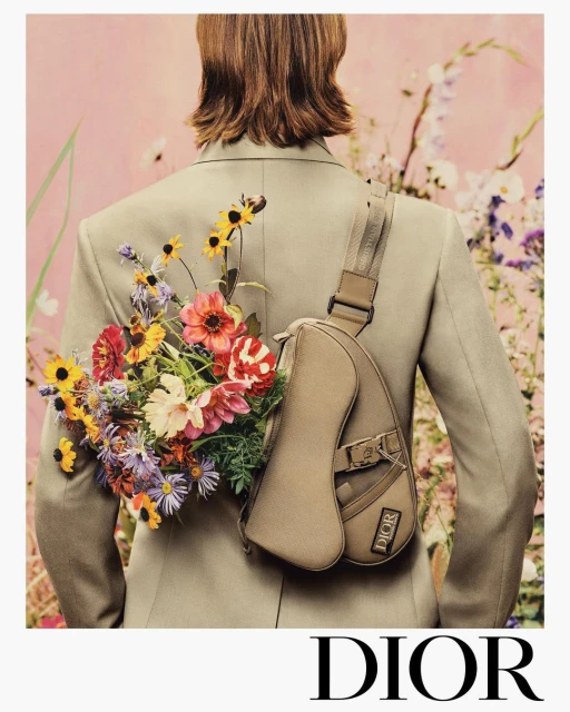 Fashion shot of a male model from the back wearing a blazer and sling bag, holding a colourful bouquet of flowers, Dior logo.