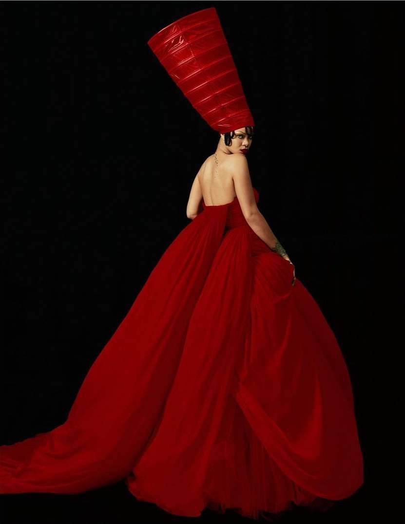 Rihanna wearing a voluminous red gown and tall headdress against a dark background, photographed by Rafael Pavarotti.