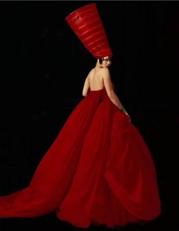 Rihanna wearing a voluminous red gown and tall headdress against a dark background, photographed by Rafael Pavarotti.
