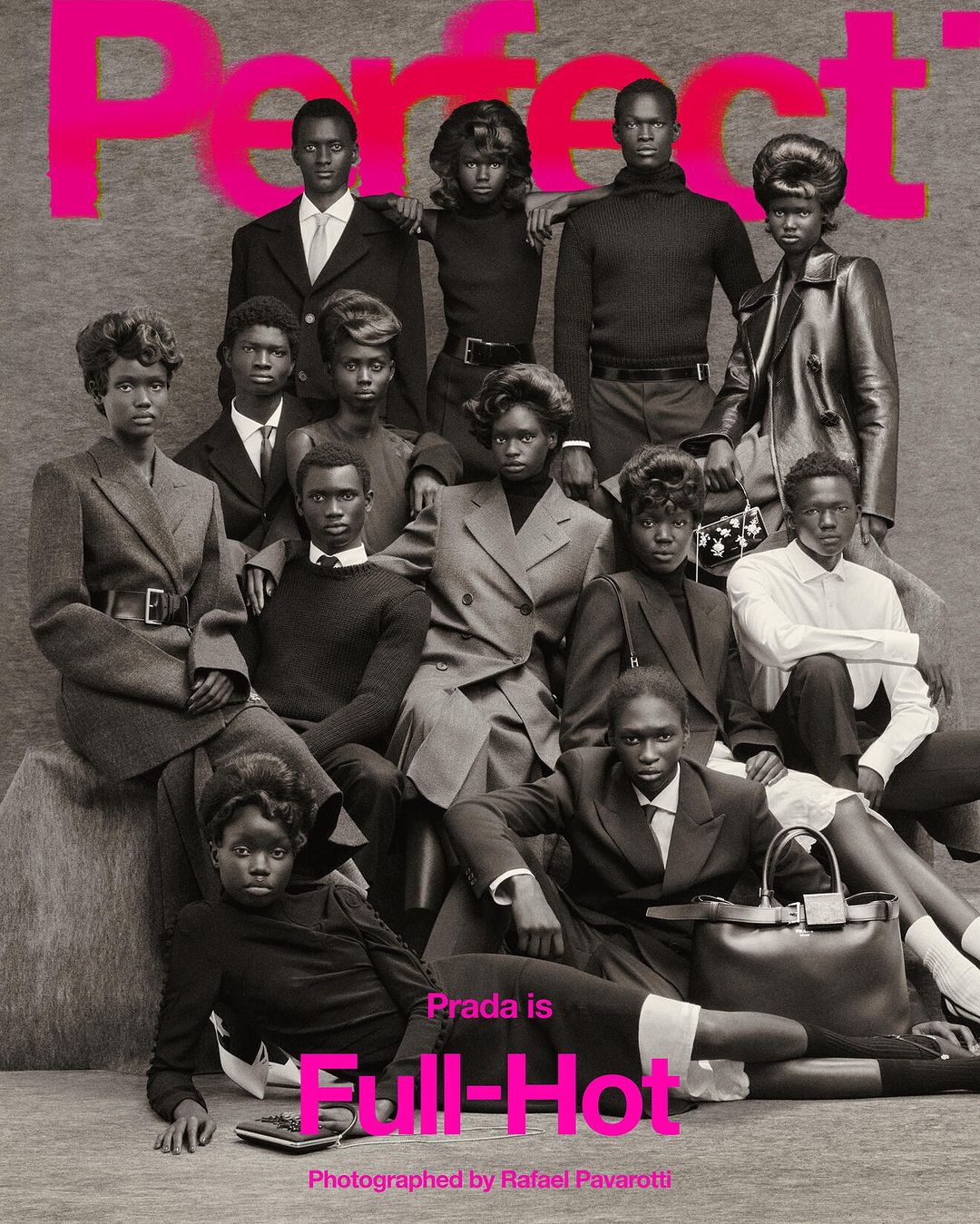 Fashion editorial shot of a group of dark-skinned models in tailored jackets and tops, some seated, in front of a gray background.
