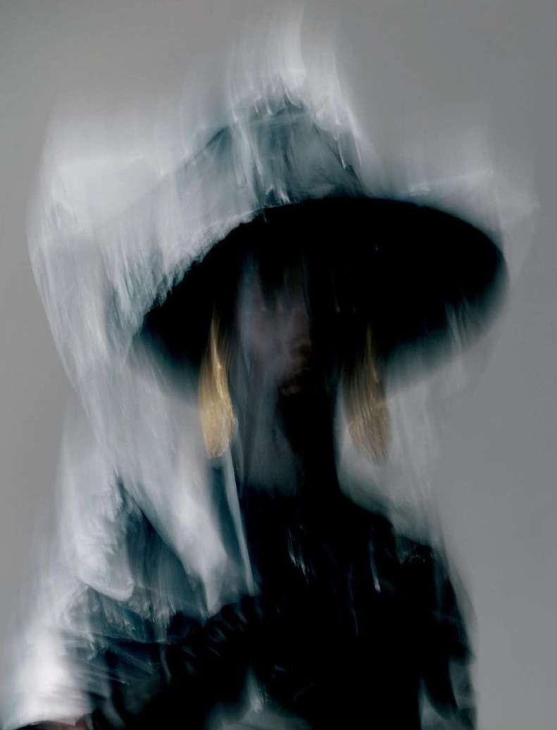 Fashion portrait of a person wearing a wide-brimmed hat and golden earrings with a blurred motion effect in a studio setting.
