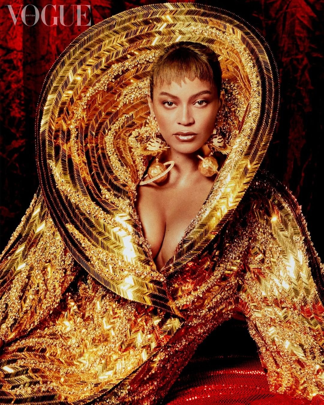 A portrait of a woman with intricate gold embellishments, large earrings, and a dramatic, ornamental collar against a dark red backdrop.