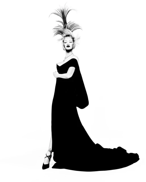 Black and white portrait of a stylish woman in a black gown with an elaborate feathered hairstyle posing against a white backdrop.