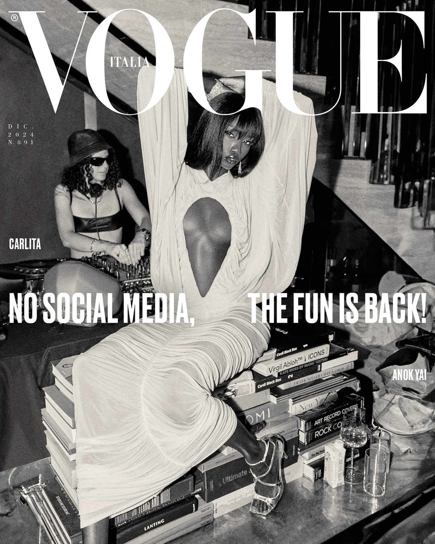 Vogue Italia cover featuring Anok Yai in a light dress, seated on books, with a DJ in the background and bold magazine typography.