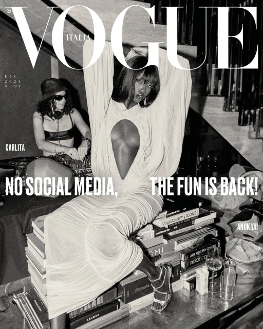 Vogue Italia cover featuring Anok Yai in a light dress, seated on books, with a DJ in the background and bold magazine typography.