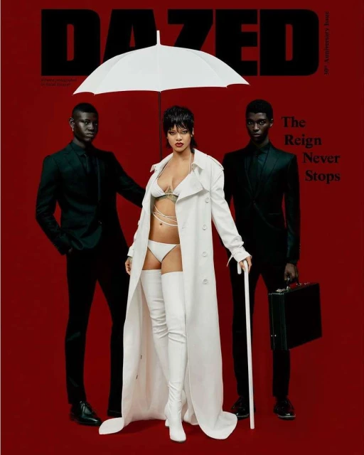 Magazine cover with Rihanna in white lingerie and trench coat, flanked by two male models in suits under an umbrella, on a red background.
