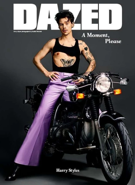 Harry Styles on a motorcycle for Dazed magazine, wearing a black tank top, lavender pants, with Dazed logo and 'A Moment, Please' text.