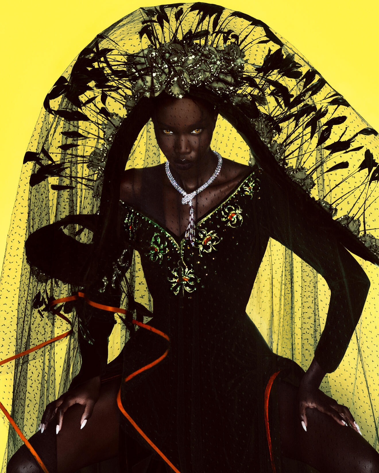 Dramatic fashion shot of a dark-skinned model in a black dress, large crown, and veil against a bright yellow backdrop.
