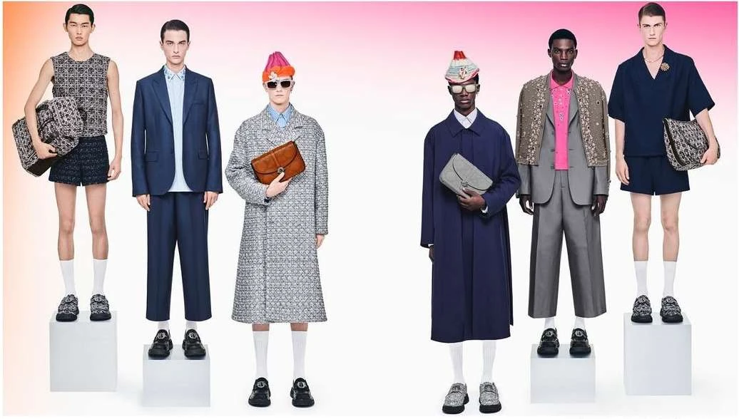 Multiple fashion models wearing outfits featuring suits, shorts, blazers, coats, hats, and bags, standing on white platforms in a studio setting.