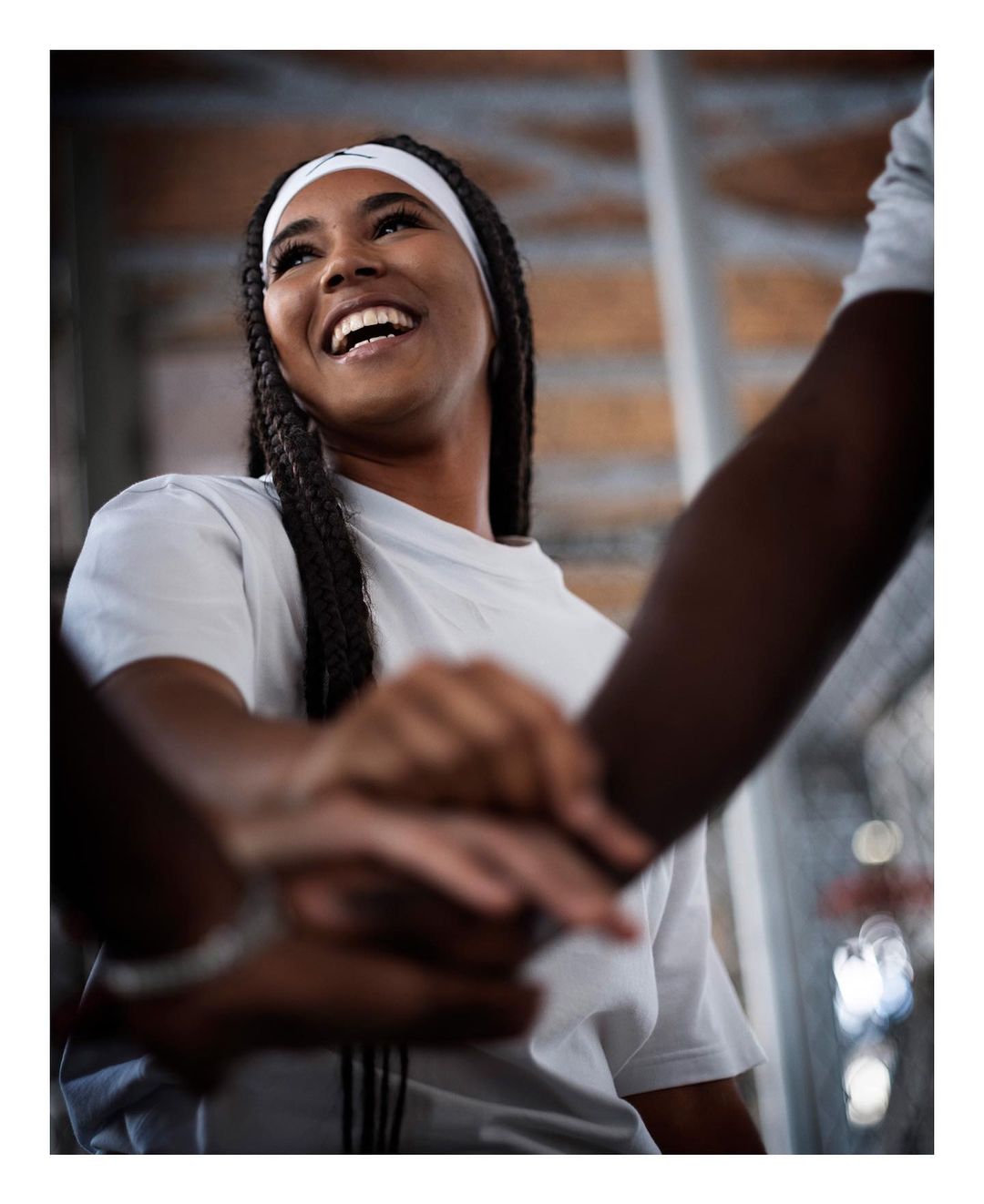 Smiling young woman with braided hair and a white headband joins hands with a group of people in a show of teamwork and collaboration.