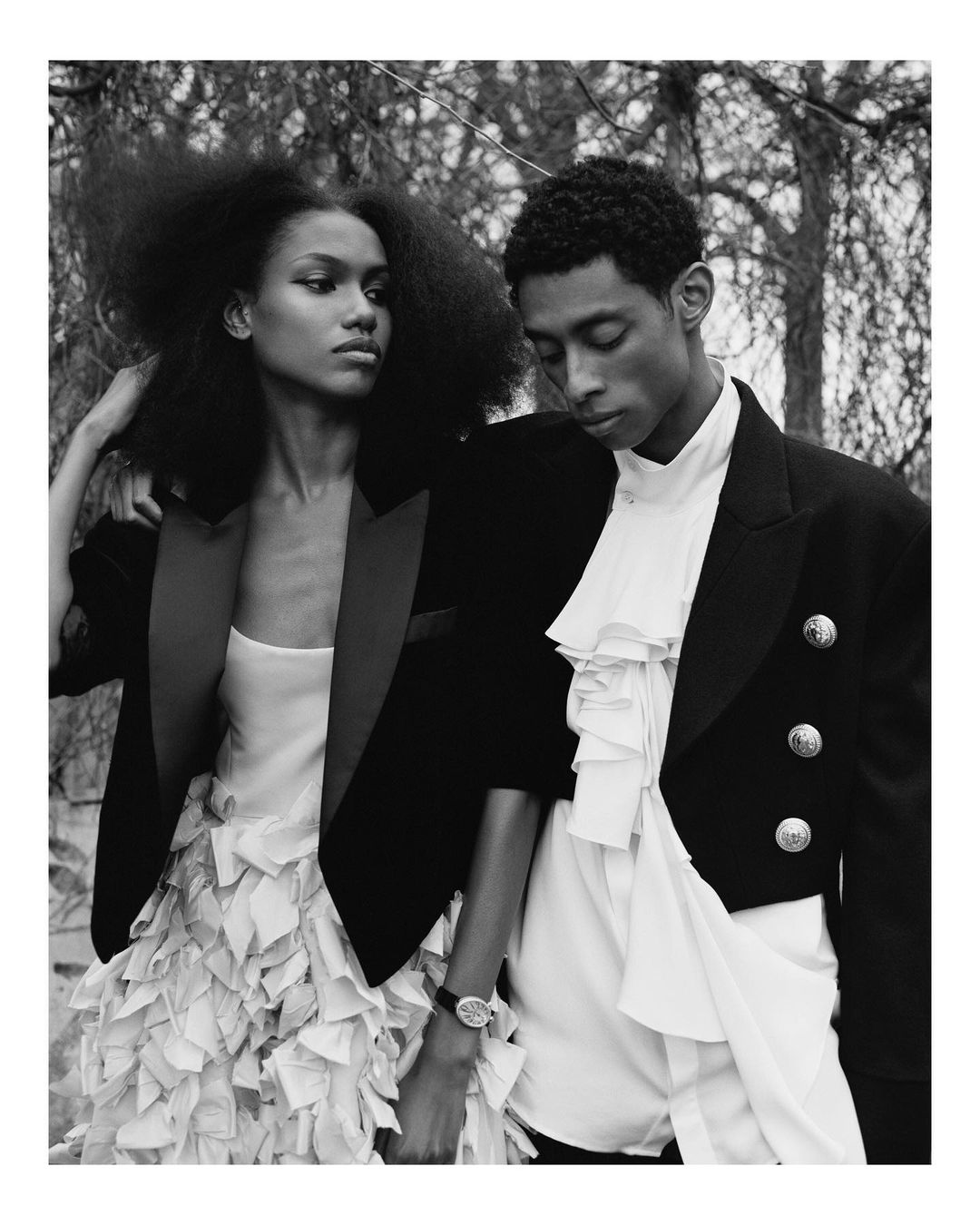 Monochrome portrait of a Black woman in a ruffled dress and a Black man in a tuxedo outdoors, captured in a fashion editorial.