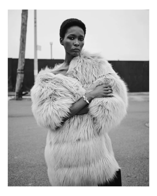 Black and white portrait of a Black woman in a furry coat outdoors against a gray sky. She is looking at the camera with a neutral expression.