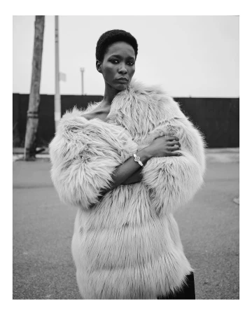 Black and white portrait of a Black woman in a furry coat outdoors against a gray sky. She is looking at the camera with a neutral expression.
