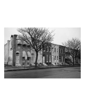 Monochrome photograph of row houses and bare trees lines a city street, evoking urban decay and somber winter atmosphere on overcast day.