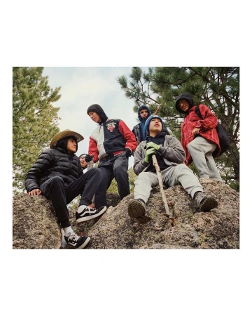 Group of young men gathers on a rock outcrop in a natural setting, wearing a variety of casual jackets, hoodies, jeans, and sneakers.