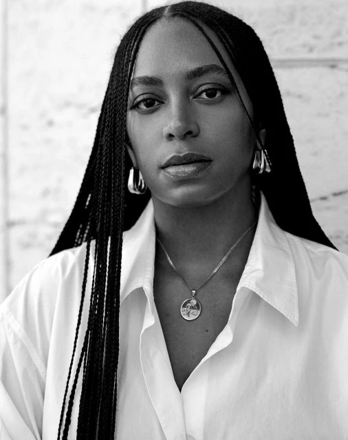 Striking black-and-white portrait of a woman with braided hair, wearing a white shirt and hoop earrings, against a textured background.