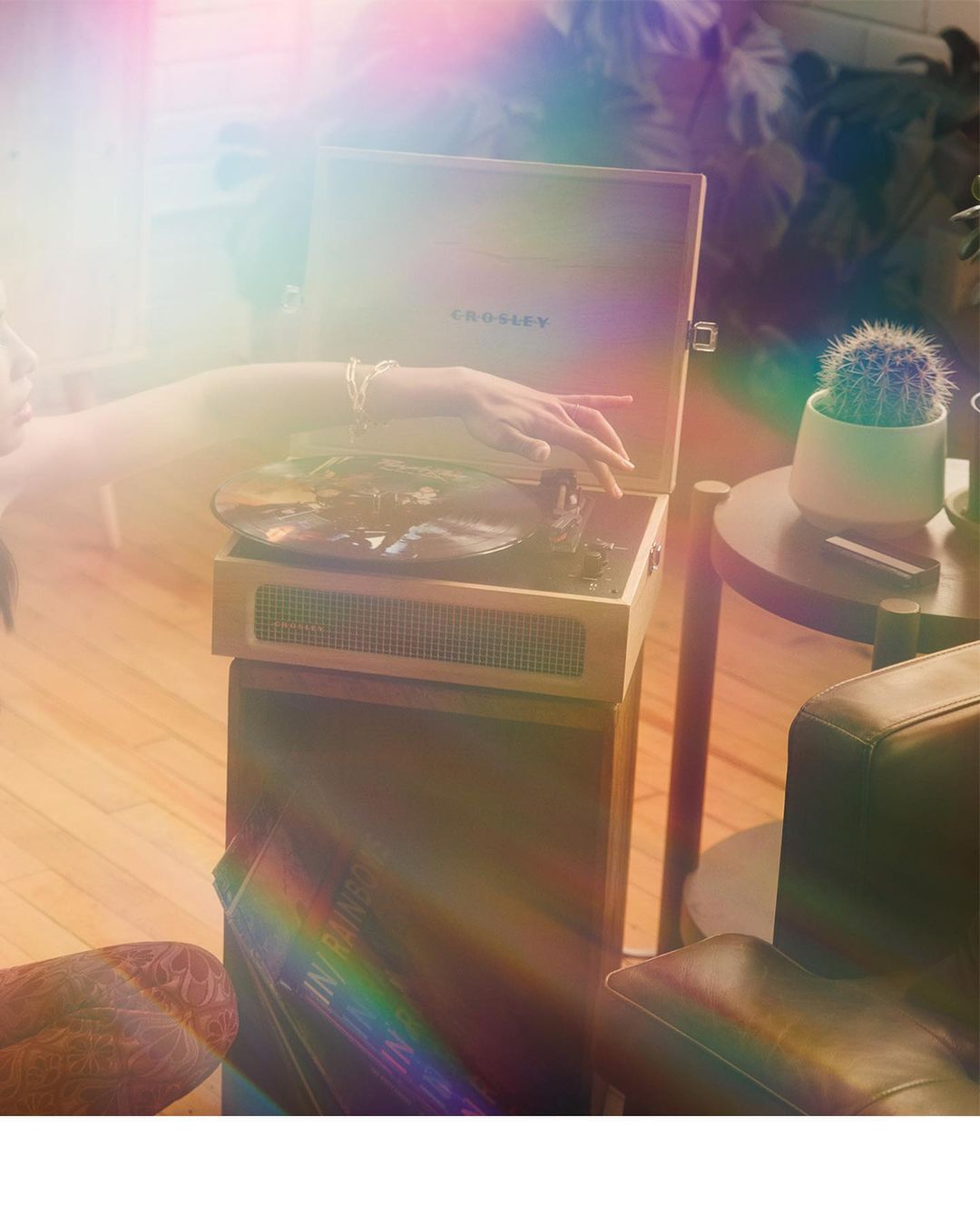 Close-up shot of a vinyl record player on a wooden stand with a record spinning and a person's hand resting near the device.