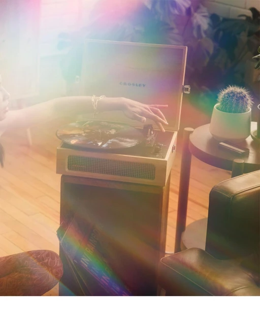 Close-up shot of a vinyl record player on a wooden stand with a record spinning and a person's hand resting near the device.