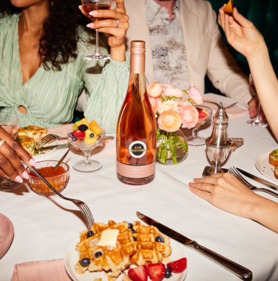 Elegant table setting with rose wine, waffles, fruit, and flowers, capturing a moment of culinary indulgence and social gathering.