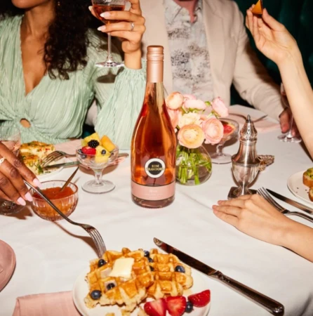 Elegant table setting with rose wine, waffles, fruit, and flowers, capturing a moment of culinary indulgence and social gathering.