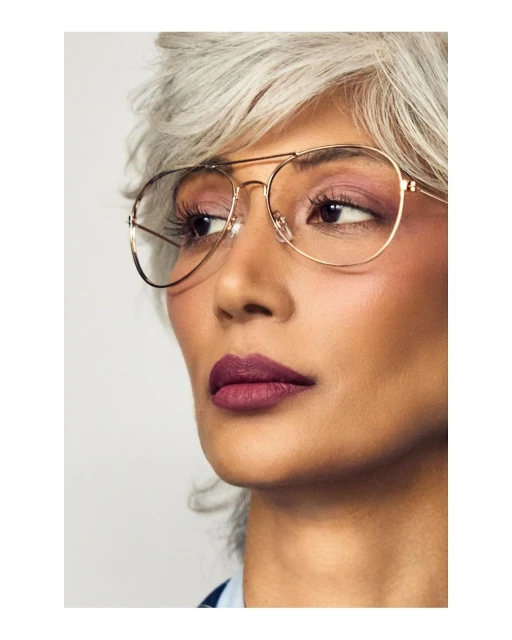 Close-up studio portrait of an adult female with gray hair and bronze-framed glasses, looking away from the camera. Beauty shot.